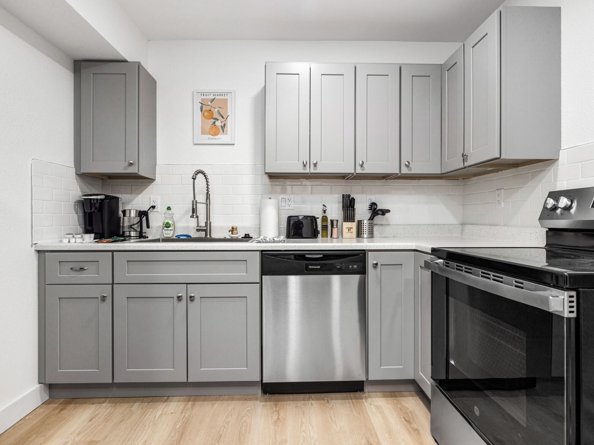 A modern kitchen with grey cabinetry, a stainless steel dishwasher, and a black oven.