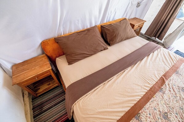 A bed with a beige and brown bedspread, two wooden nightstands, and a small wooden table. - Butterfly Bali Glamping (Baturiti)