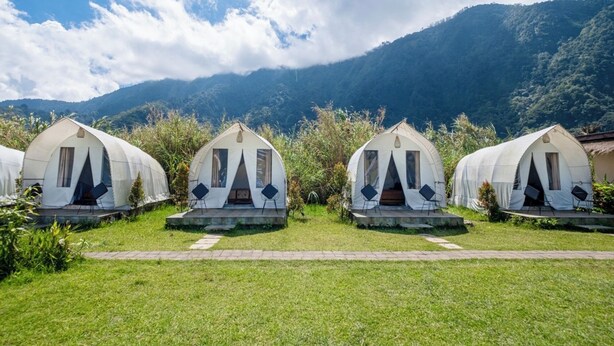 A row of dome-shaped tents with individual seating areas, set against a backdrop of lush green hills and a partly cloudy sky. - Butterfly Bali Glamping (Baturiti)