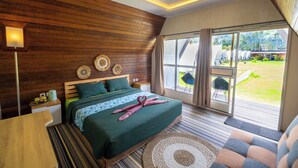 A bedroom with a wooden wall, a bed with green bedding, a bedside table, a lamp, and a view of the outdoors. - Butterfly Bali Glamping (Baturiti)