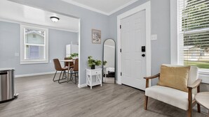 A modern living room with a dining area, a white door, and a window with blinds. - Sunny Pensacola Studio Near Beach & Downtown (Pensacola)