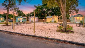 A row of small, single-story cabins with picnic tables in front, set against a backdrop of trees and a twilight sky. - Sunny Pensacola Studio Near Beach & Downtown (Pensacola)