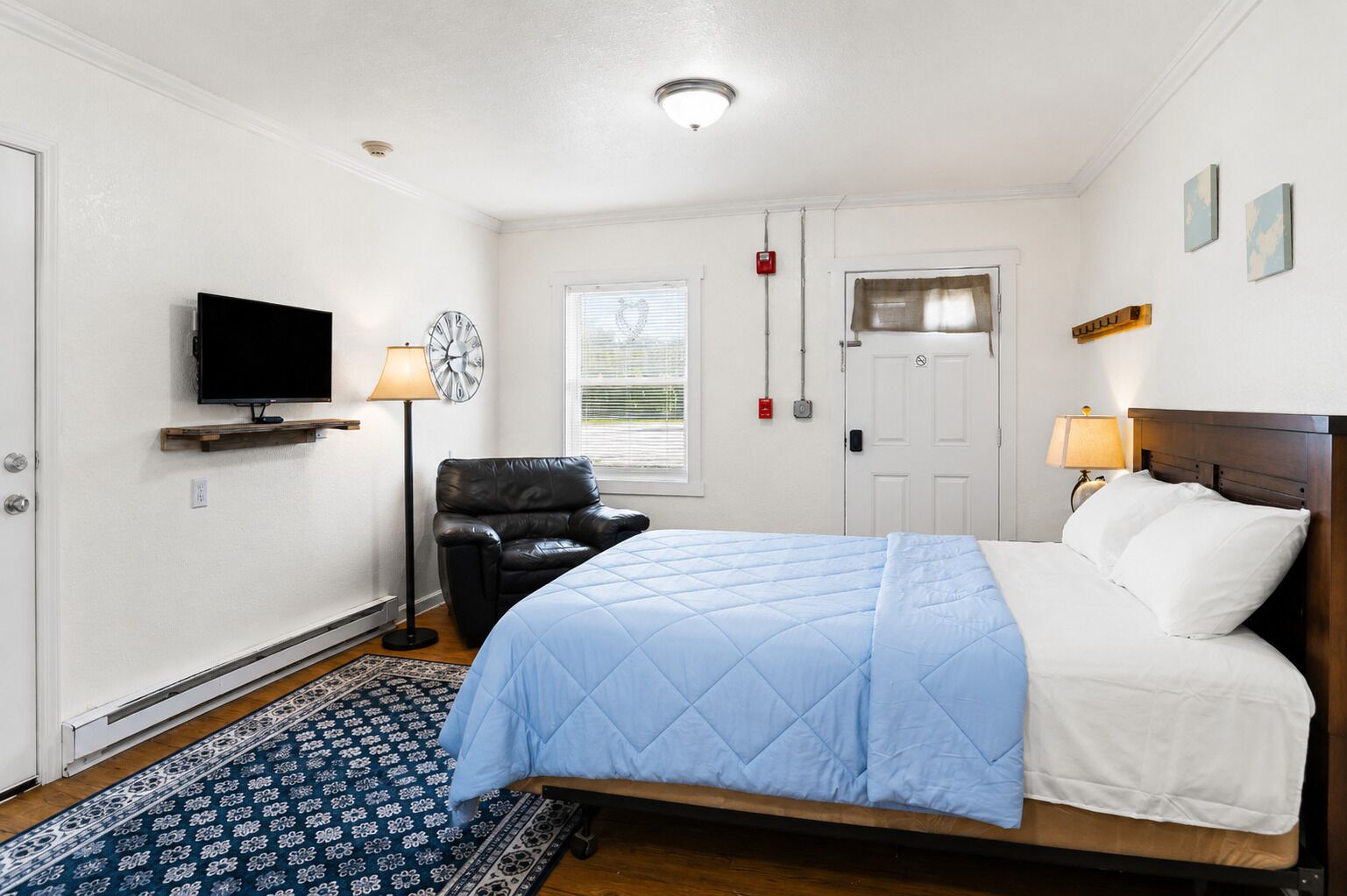 A bedroom with a bed, a chair, a TV, a window, and a door.