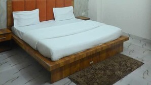 A bedroom with a bed, wooden headboard, white bedding, a ceiling fan, patterned wallpaper, and a tiled floor. - Hotel Shiv Kripa (Kanpur)