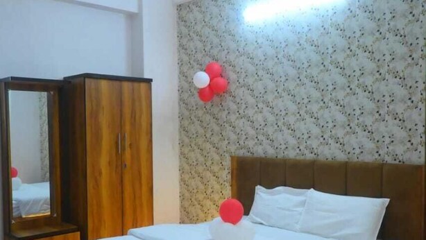 A bedroom with a bed, a wardrobe, a ceiling fan, and a wall with floral wallpaper and balloons. - Hotel Shiv Kripa (Kanpur)