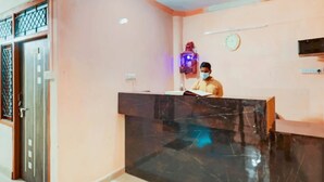 A reception desk with a person seated behind it, a clock on the wall, and a door with a metal gate to the left. - Hotel Shiv Kripa (Kanpur)