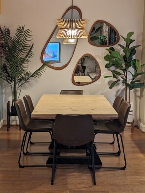 A dining area with a wooden table, six chairs, a hanging light fixture, and two wall-mounted mirrors. - Serene Desert Villa-4 bedrooms, pool and hot tub (Palm Springs)
