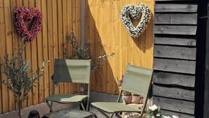 A wooden fence with heart-shaped decorations, two green chairs, and potted plants. - Cottage - Sleeps 4 - Pets Ok - Garden - Parking (Middlewich)