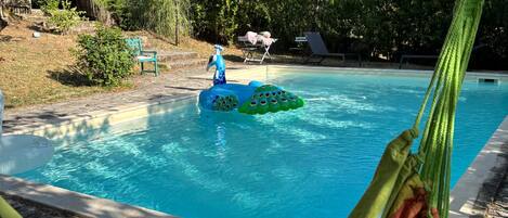 Una cadira d'hamaca sobre una piscina, amb un joguet flotant i gandules al fons.