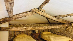 A rustic bedroom with two wooden beds, a stone wall, and a sloped ceiling supported by wooden beams. - 2 Bedroom Cottage - Sleeps 6 - Pool - Garden (Caylus)