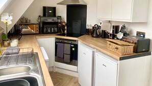 A modern kitchen with a built-in oven, a coffee machine, and a stove. There is a small dishwasher and a sink with a dish rack. - Central Tenby 3 Bed Apt Sleeps 6 to 8 Dog Friendly (Pembrokeshire)