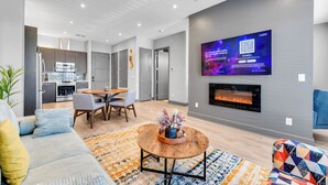 Una sala de estar moderna con un televisor de pantalla plana en la pared, una chimenea y un comedor con mesa y sillas.