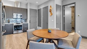 Una cocina moderna con armarios grises, electrodomésticos de acero inoxidable y una mesa de madera redonda con cuatro sillas.
