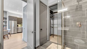 Un baño moderno con cabina de ducha de vidrio, pared con azulejos grises y cabezal de ducha visible.