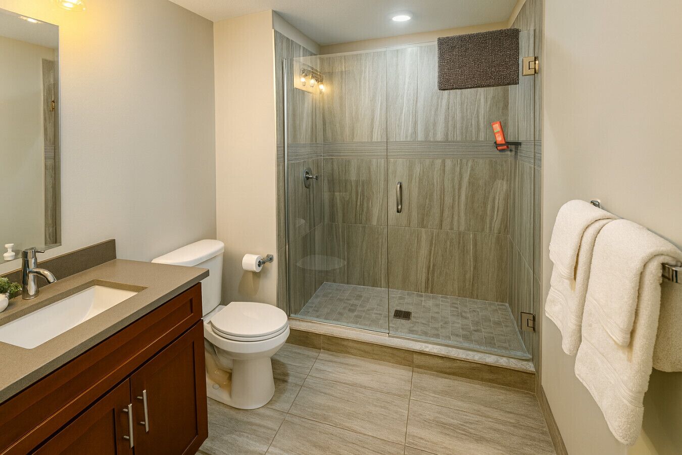 Un baño moderno con cabina de ducha de vidrio, lavamanos con espejo e inodoro.