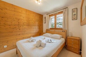 Habitació amb panells de fusta, un llit, una tauleta de nit, una finestra amb cortines i un quadre penjat a la paret.