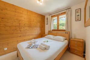 A wooden-paneled room with a bed, a nightstand, a window with curtains, and a wall-mounted picture.