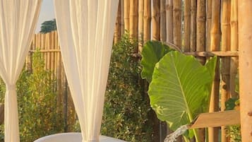 A white bathtub with a bamboo fence and large green leaves in the background.