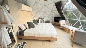Une chambre à coucher avec un lit, une table de chevet, une lampe et une vue dégagée sur l’extérieur grâce à de grandes fenêtres.
