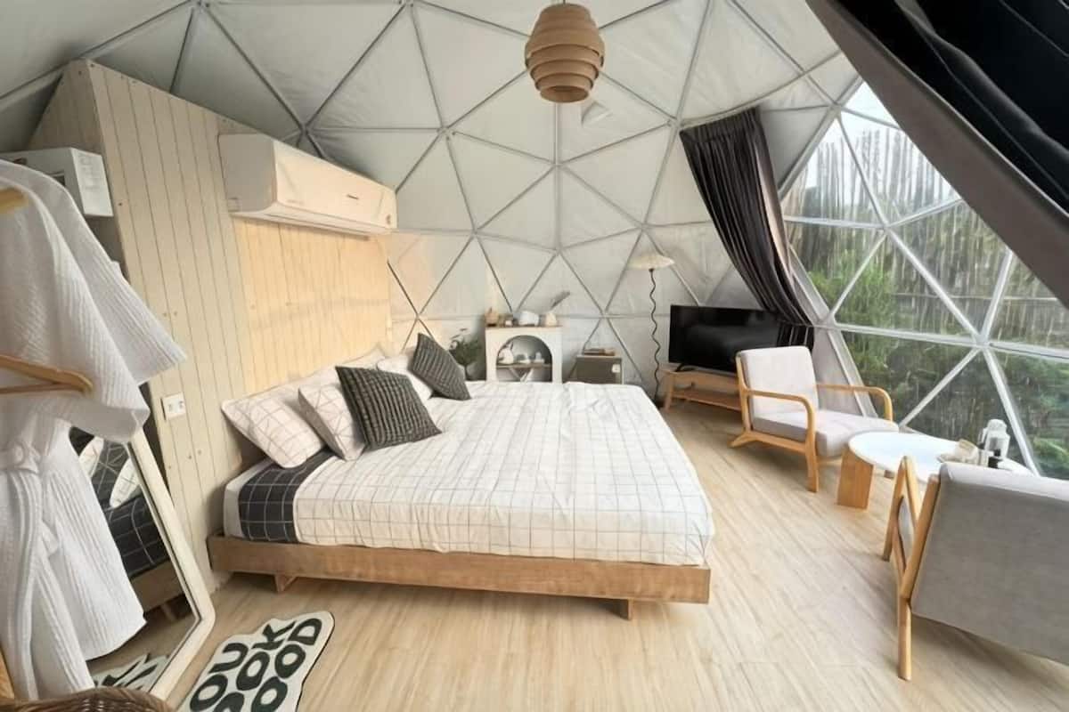 A bedroom with a bed, bedside table, lamp, and a view through large windows.