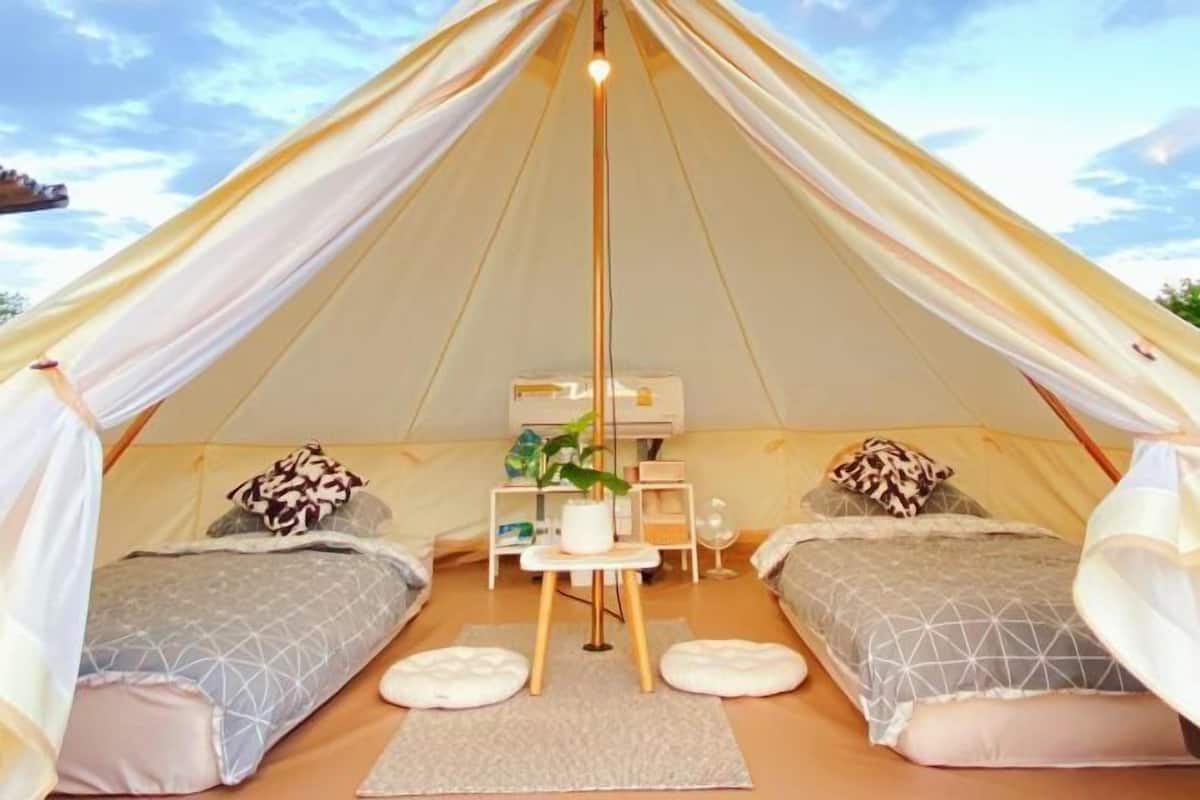 A tent with two beds, a small table with a plant, and a hanging light fixture.