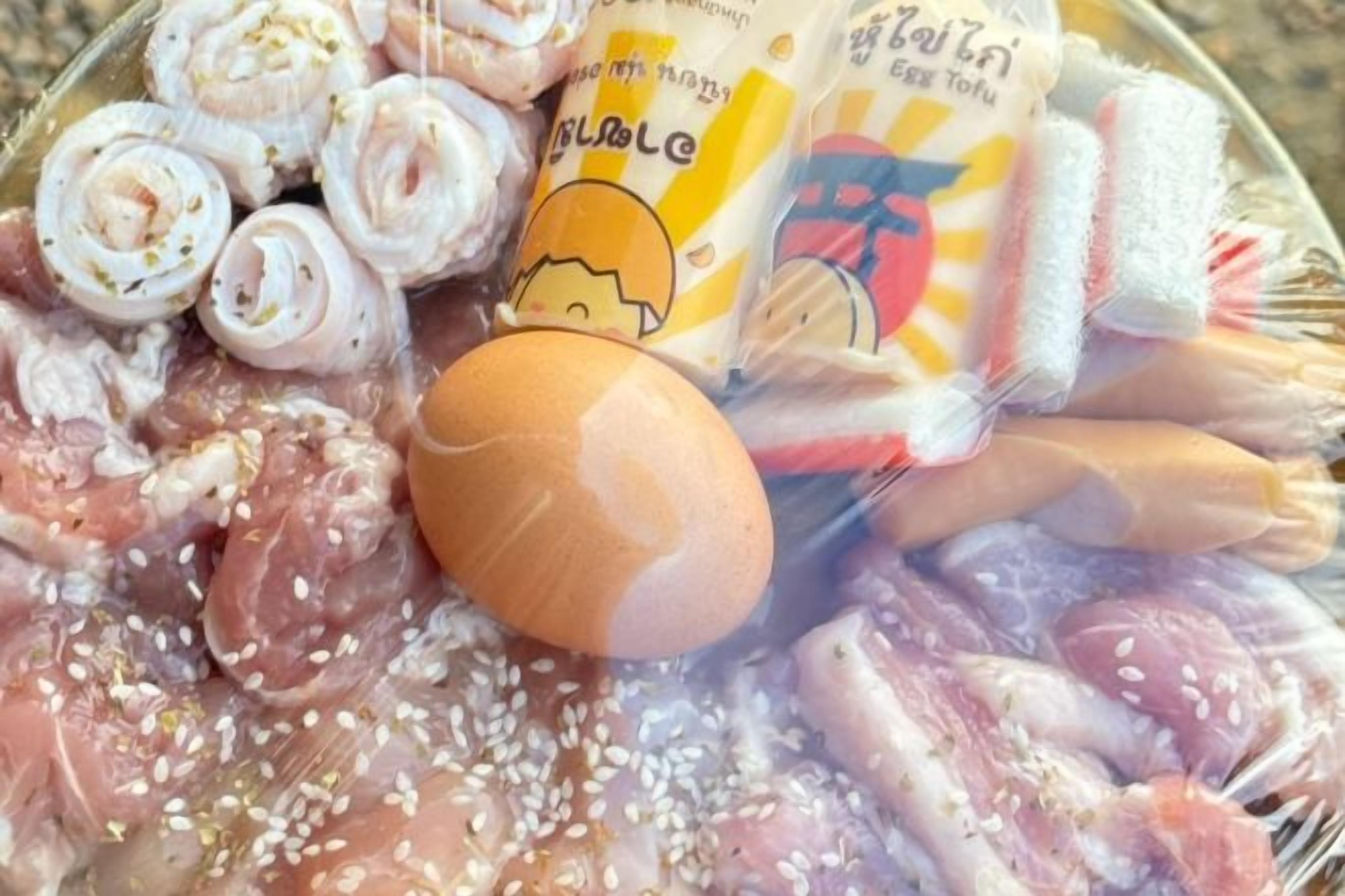 Diversos pedaços de frango cru e um ovo inteiro em uma superfície.