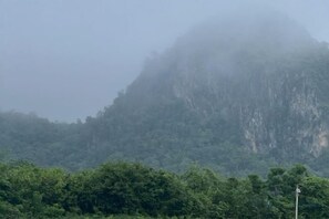 A mountainous landscape with dense greenery and a road sign in the foreground. - Khao Poon Camping (Kanchanaburi)