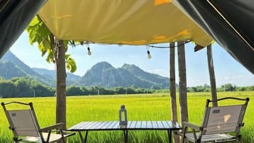A tent with a table and chairs overlooking a green field and mountains.