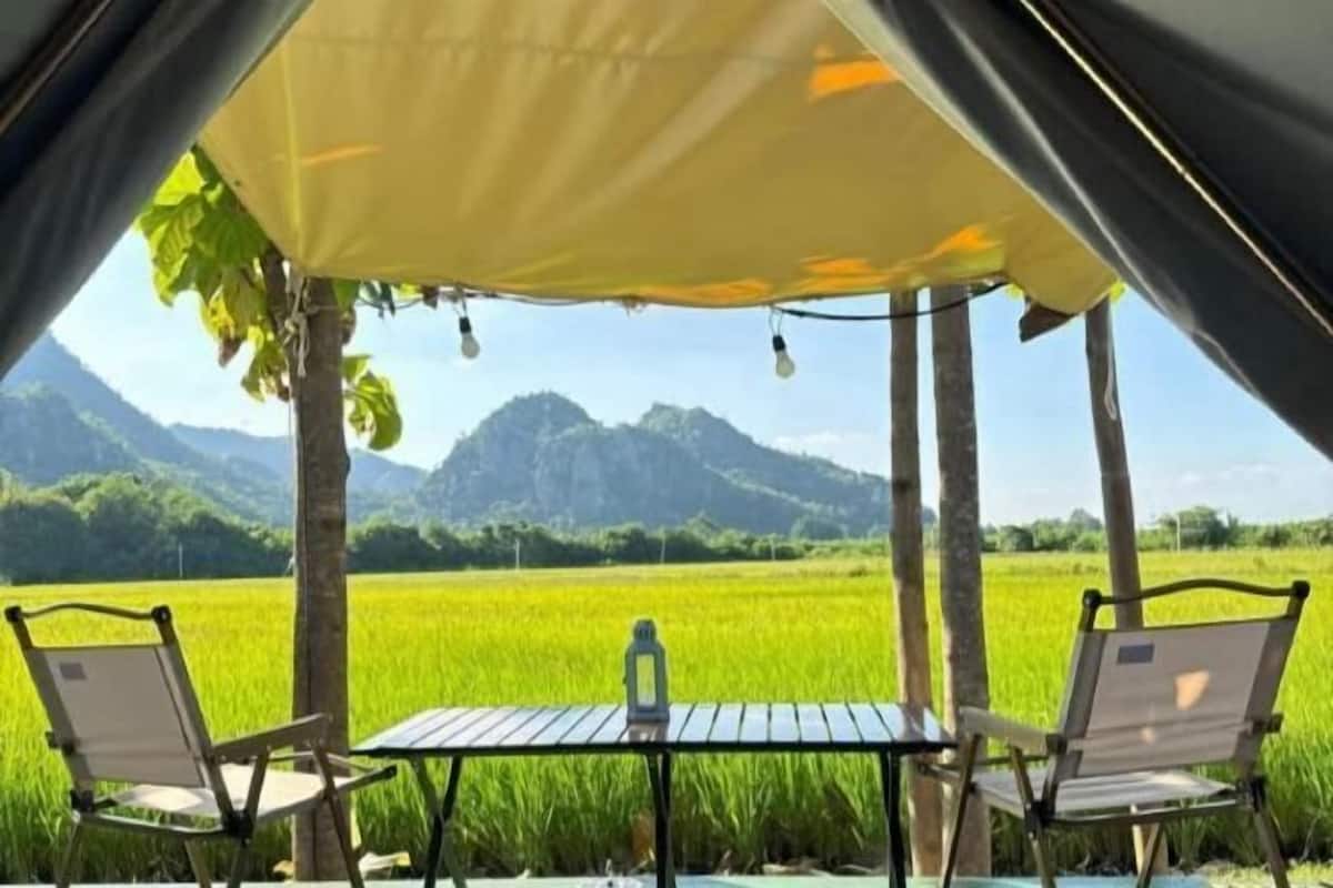 A tent with a table and chairs, overlooking a green field and mountains.