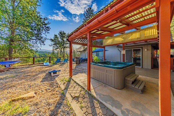 A covered outdoor area with a hot tub, seating, and a view of the landscape.