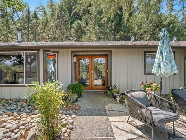 A house with a front porch, a wooden door, and a small garden area with rocks and plants.