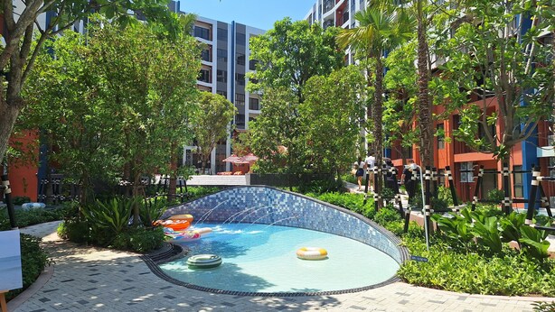 Ein Swimmingpool mit einer gefliesten Kante, umgeben von Grünflächen und modernen Gebäuden.