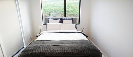 Un dormitorio con una cama grande, una ventana con vistas a la vegetación y una pequeña mesa con sillas.