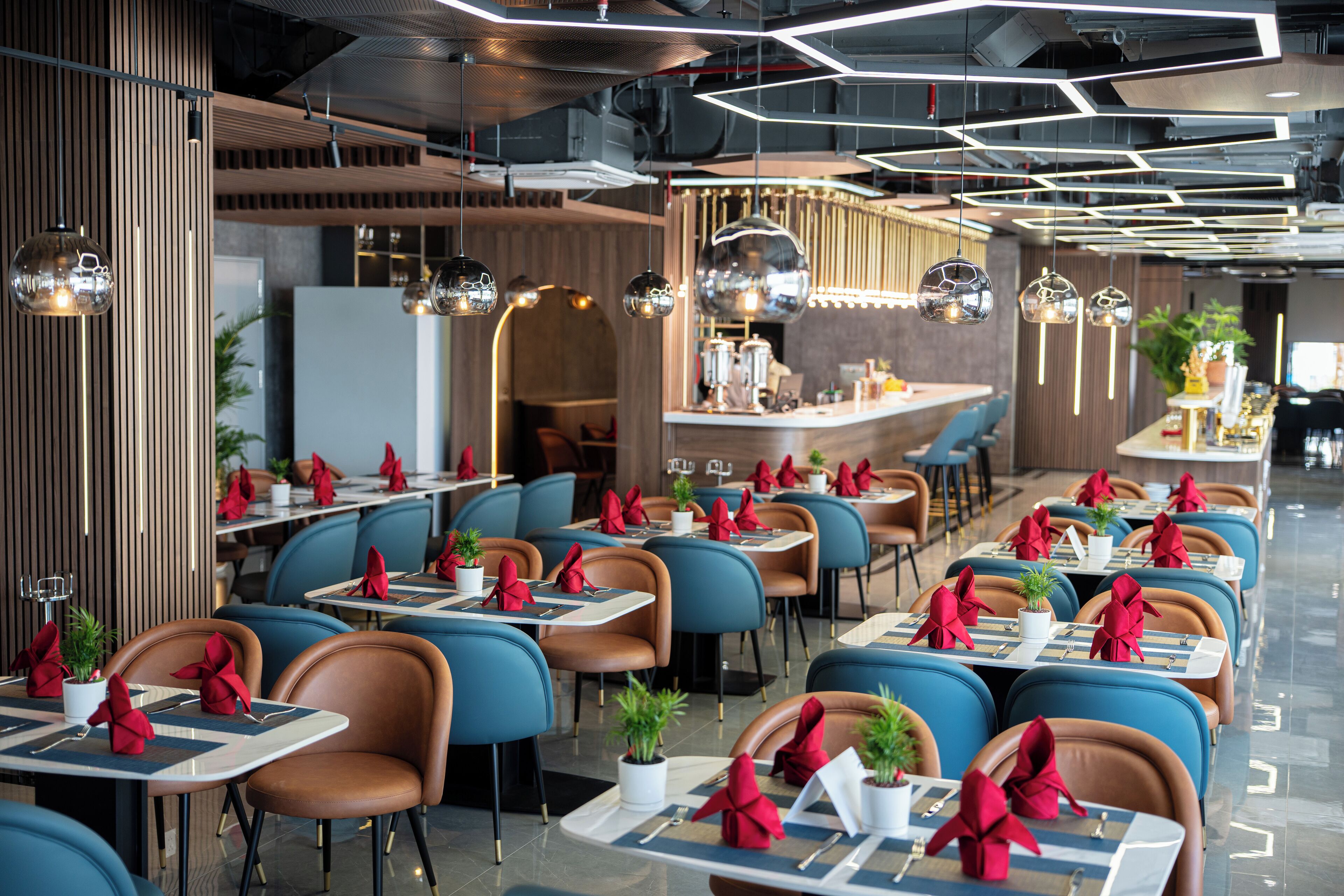 Een modern restaurant met meerdere tafels, blauw- en bruine stoelen en rode servetten.