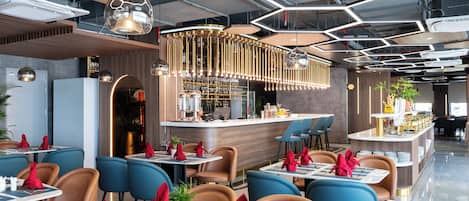 Un restaurant moderne doté d’un bar central, de chaises bleues et brunes, et d’un plafond au design géométrique.