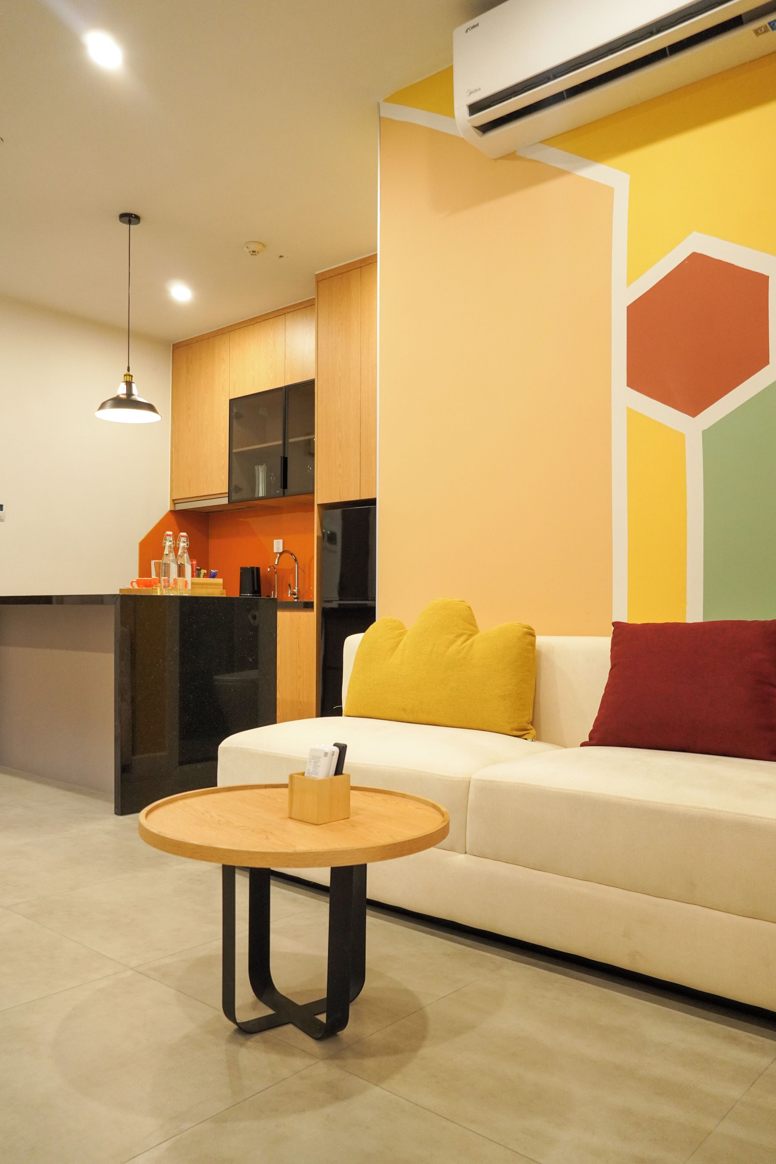 A modern living room with a sofa, a round wooden coffee table, and a kitchen area with cabinets and an air conditioning unit.