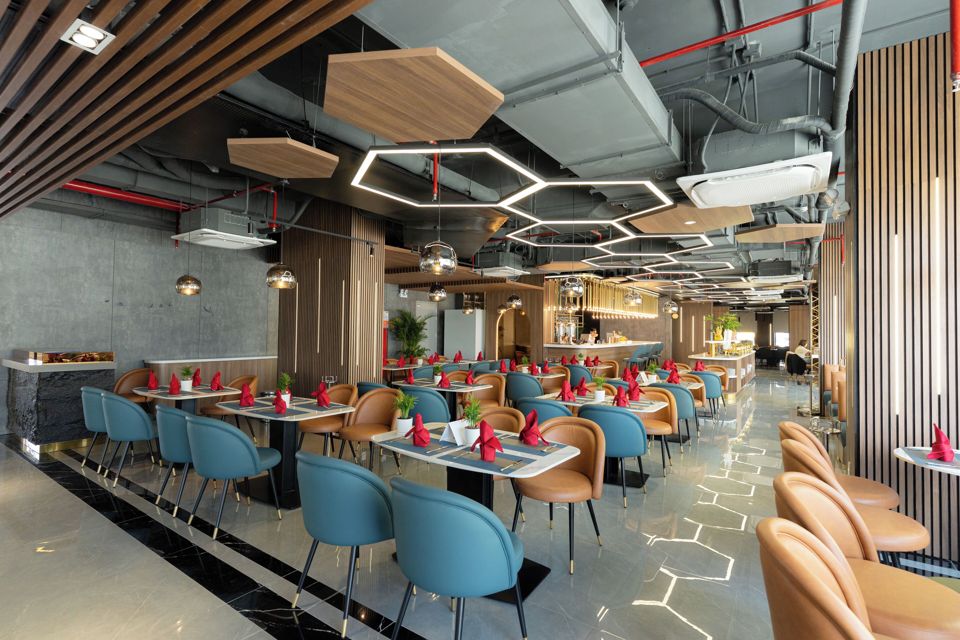 A modern restaurant with hexagonal ceiling lights, blue and brown chairs, and a polished floor.