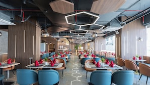 A modern restaurant with hexagonal ceiling lights, blue and brown chairs, and neatly arranged tables with red napkins. - Bcons City Hotel (Ho Chi Minh City)