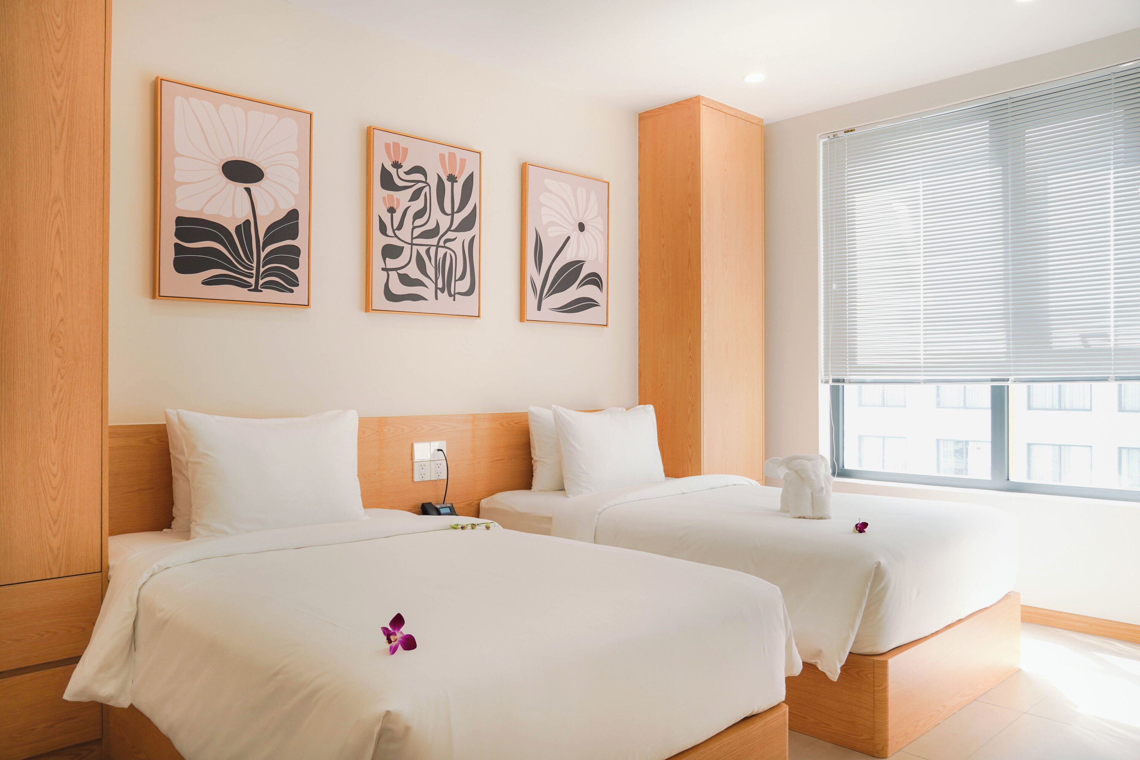 A hotel room with two beds, a wooden headboard, and three framed floral artworks on the wall.