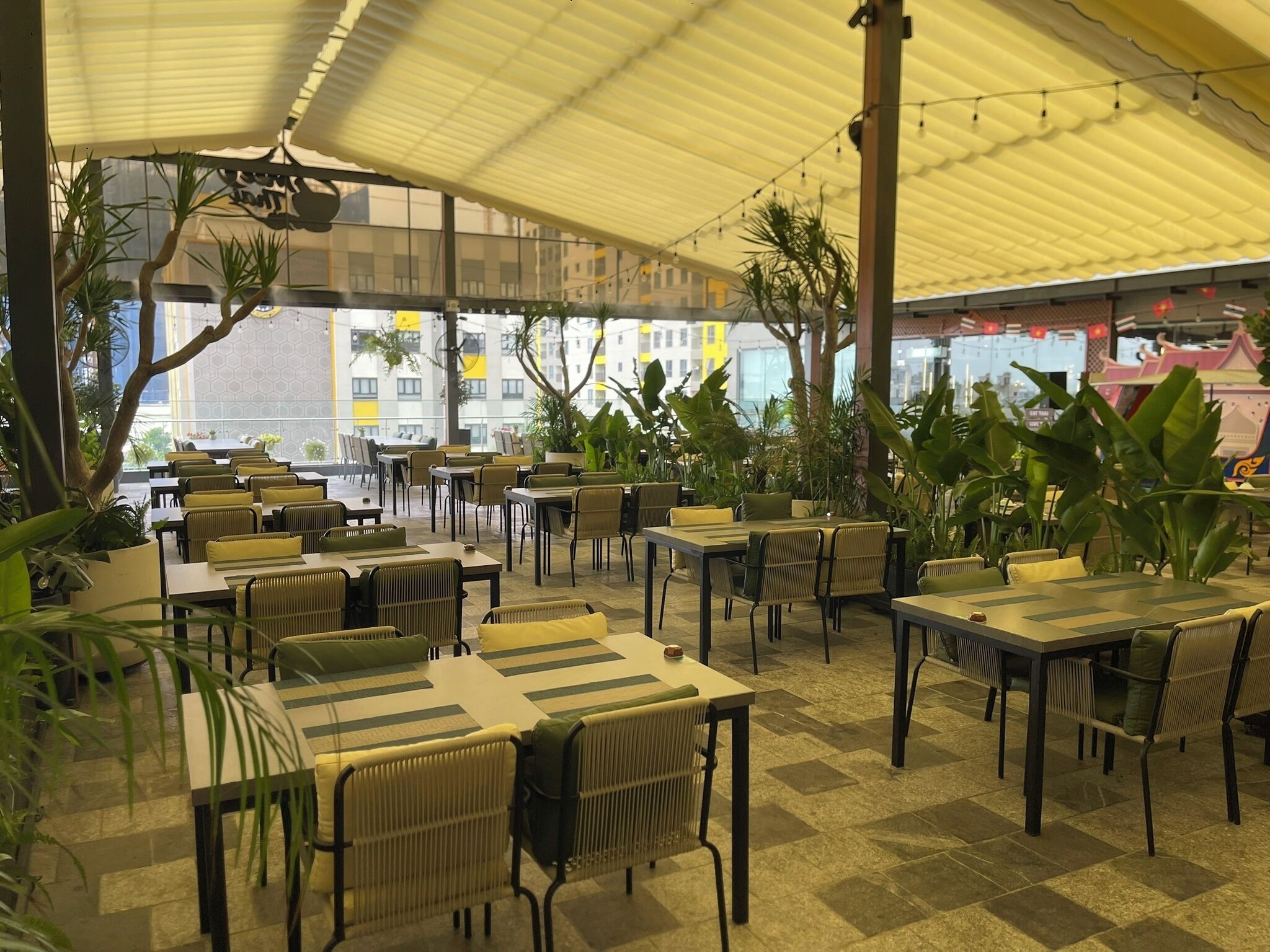 Un café al aire libre con mesas y sillas, rodeado de macetas con plantas.