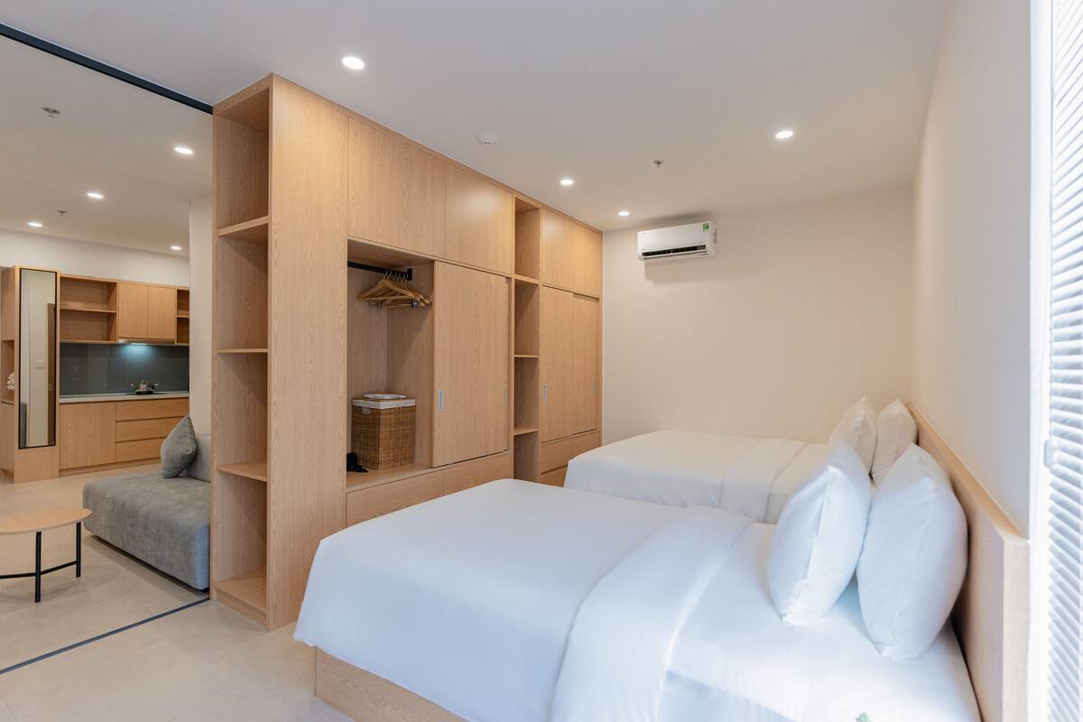 A modern hotel room with two beds, a sofa, a small table, and built-in wardrobes.