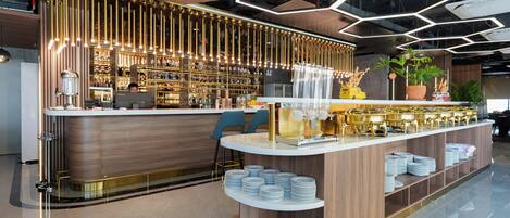 Un área de bar moderna con mostrador de madera, estantes llenos de vasos y una estación de barista.
