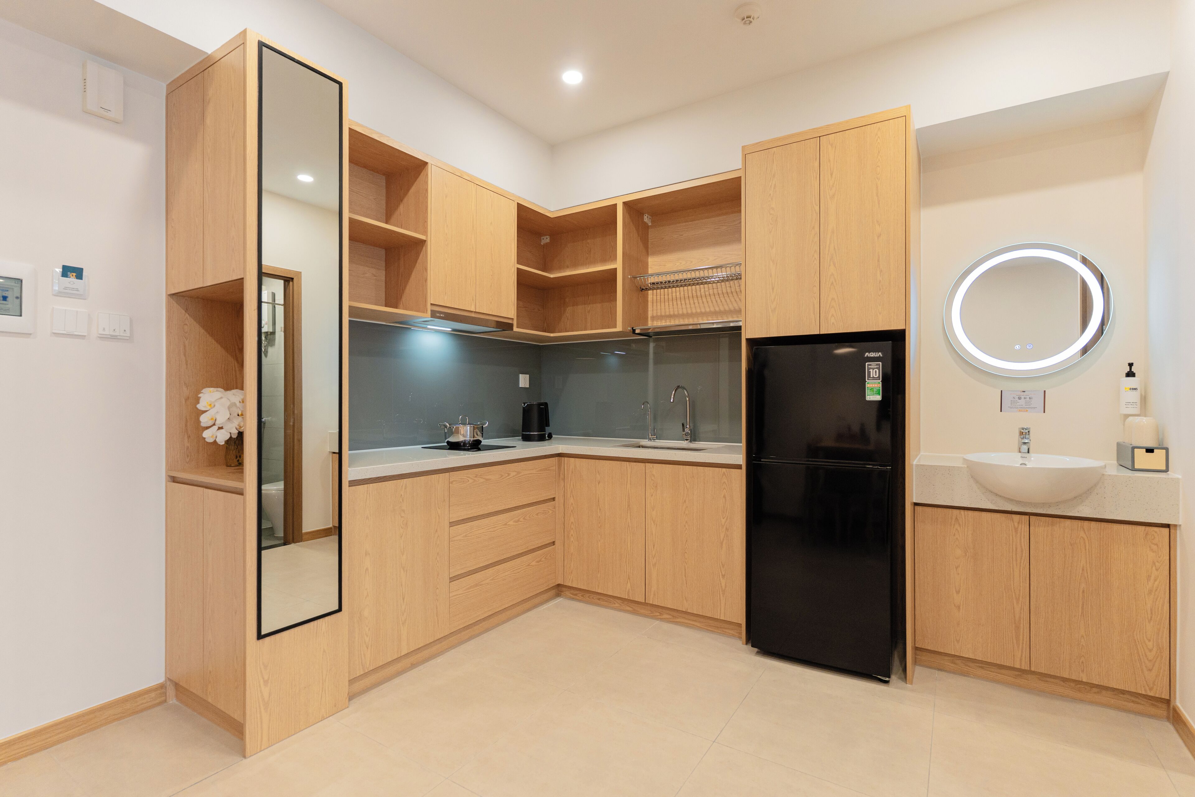 A modern kitchen with wooden cabinets, a black refrigerator, a sink with a mirror, and a coffee maker.