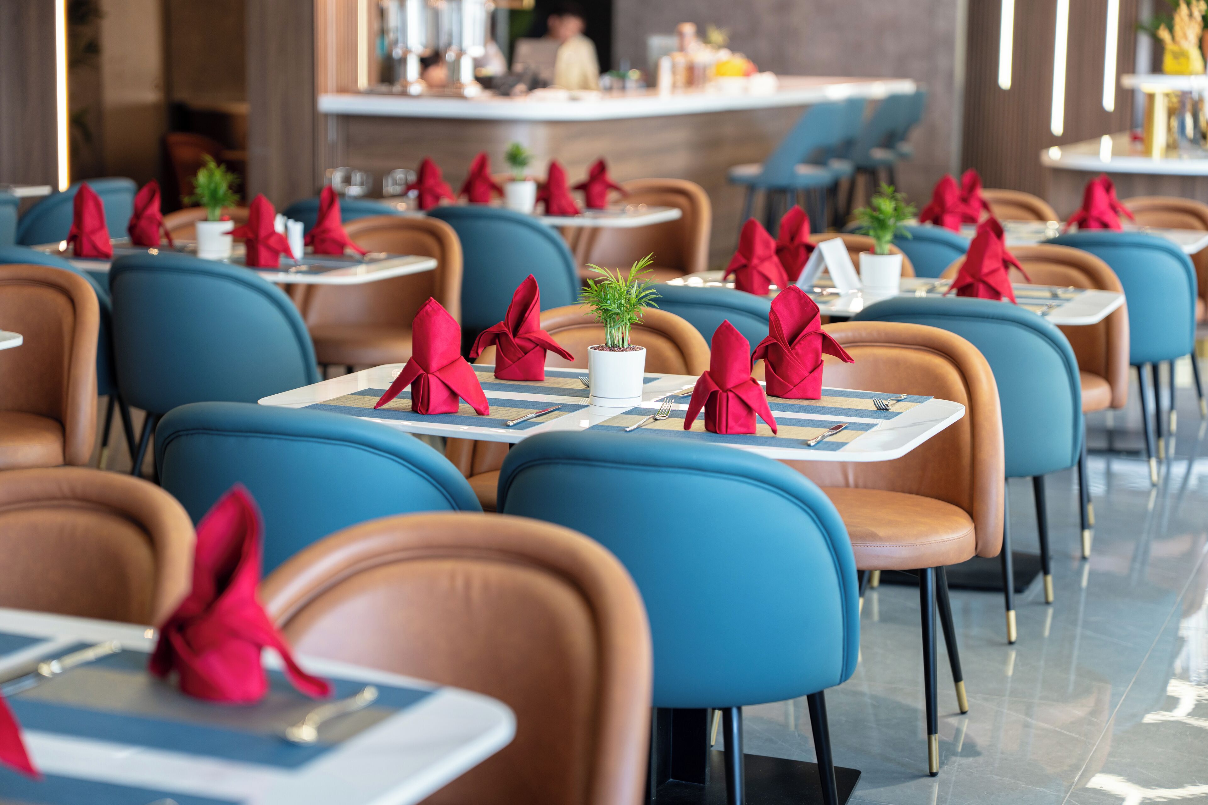 A restaurant with blue chairs and tables, each with a red napkin tied in a bow.