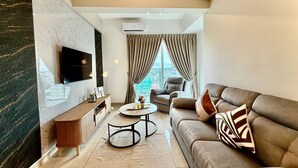 Una sala de estar moderna con un sofá, una mesa de centro, un televisor montado en la pared y vistas de la ciudad a través de amplios ventanales.