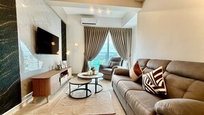 Una sala de estar moderna con un sofá de cuero, una mesa de centro, un televisor montado en la pared y un ventanal con cortinas.