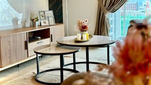 Una sala de estar moderna con una mesa redonda, un televisor en la pared y vistas a la ciudad a través de grandes ventanales.