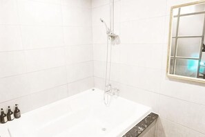 Un baño con una bañera blanca, ducha y ventana con vistas.