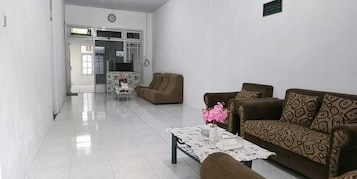 Uma sala de estar ampla com um sofá, uma mesa de centro com um vaso e uma área de jantar ao fundo.