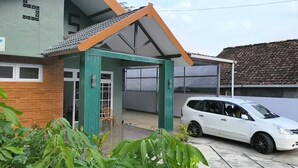 Ein Haus mit überdachter Veranda, ein weißes Auto davor und eine Ziegelmauer.